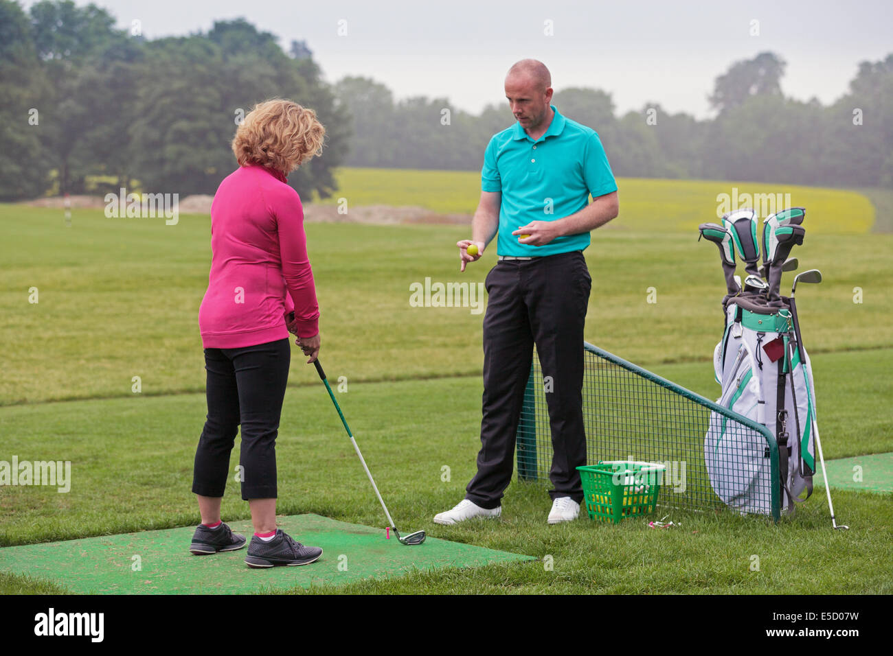 Un golfeur dame est enseigné à jouer au golf par un Pro sur une pratique d'entraînement. Banque D'Images