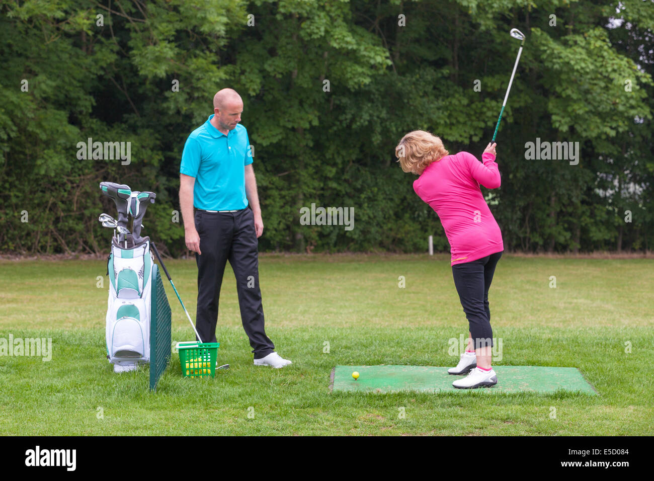 Un golfeur dame est enseigné à jouer au golf par un Pro sur une pratique d'entraînement. Banque D'Images