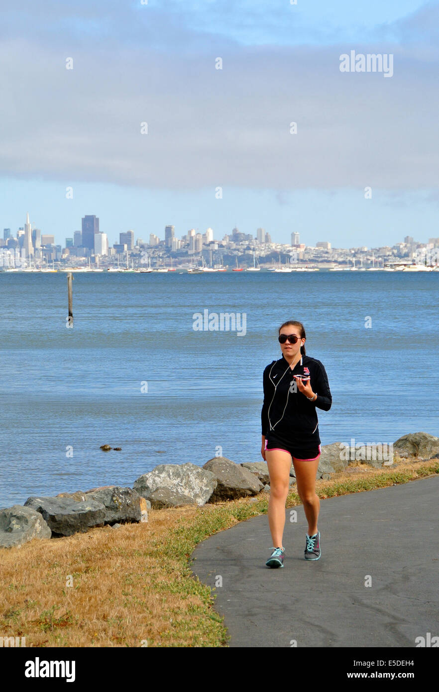 Woman jogging avec téléphone cellulaire à l'écoute de i tunes sur sentier de jogging Banque D'Images