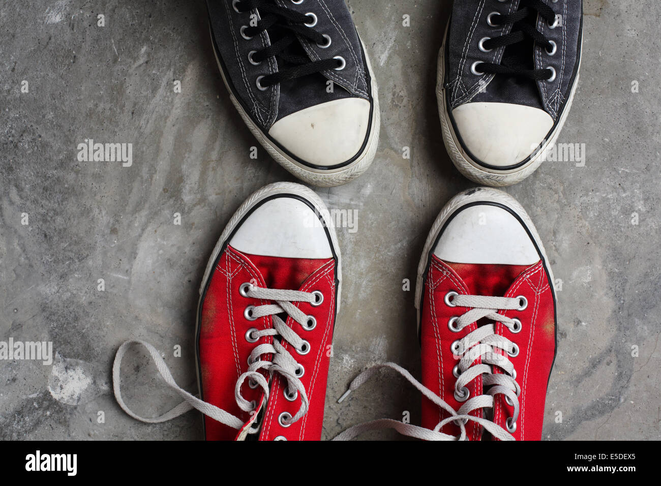 Deux paires de chaussures Converse, toe à toe, tourné contre un arrière-plan en béton Banque D'Images
