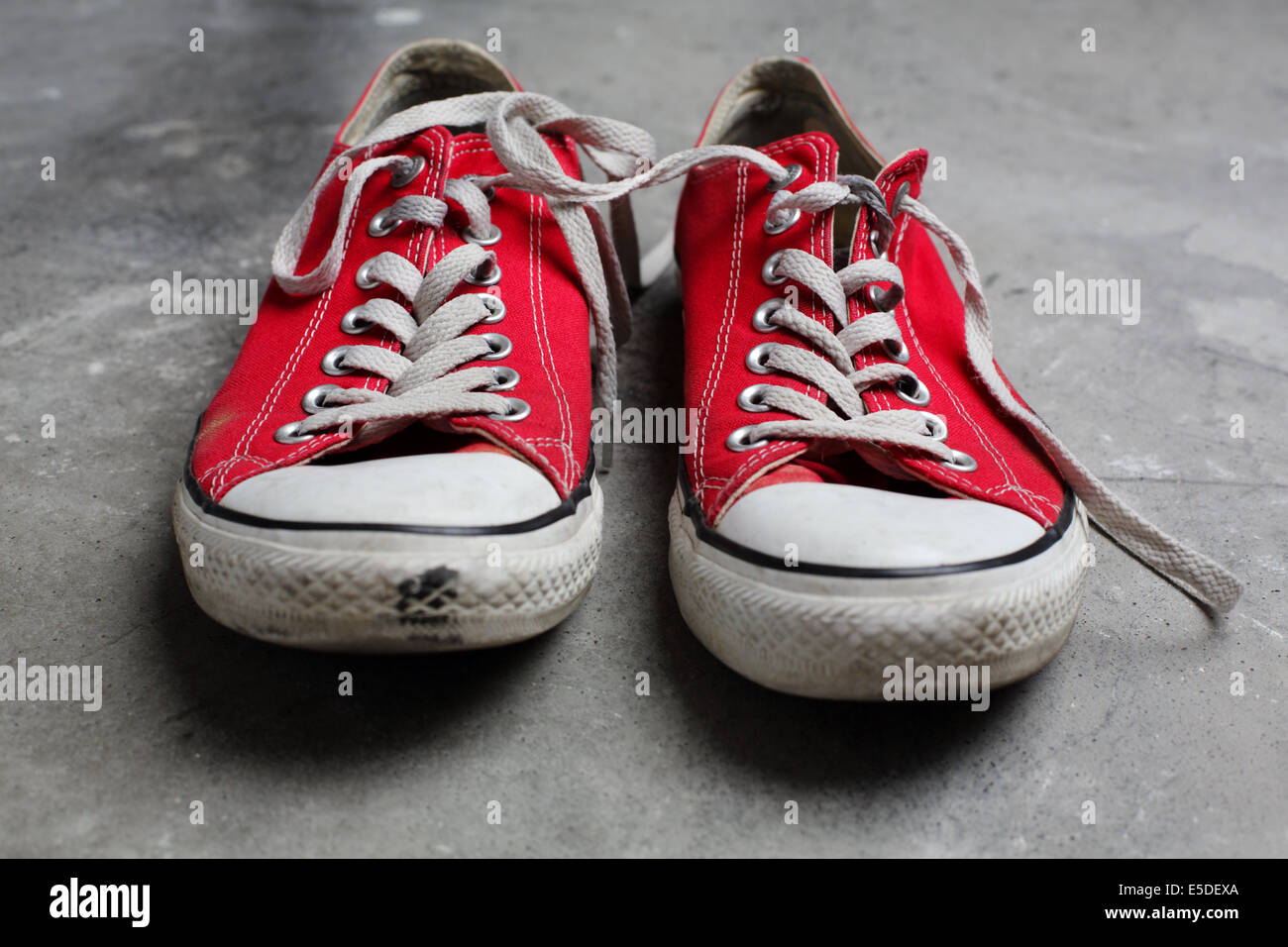 Une seule paire de chaussures Converse rouge tourné contre un arrière-plan en béton Banque D'Images