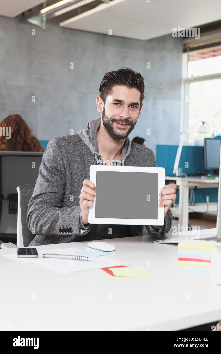 Portrait of smiling man showing tablet ordinateur dans le bureau Banque D'Images