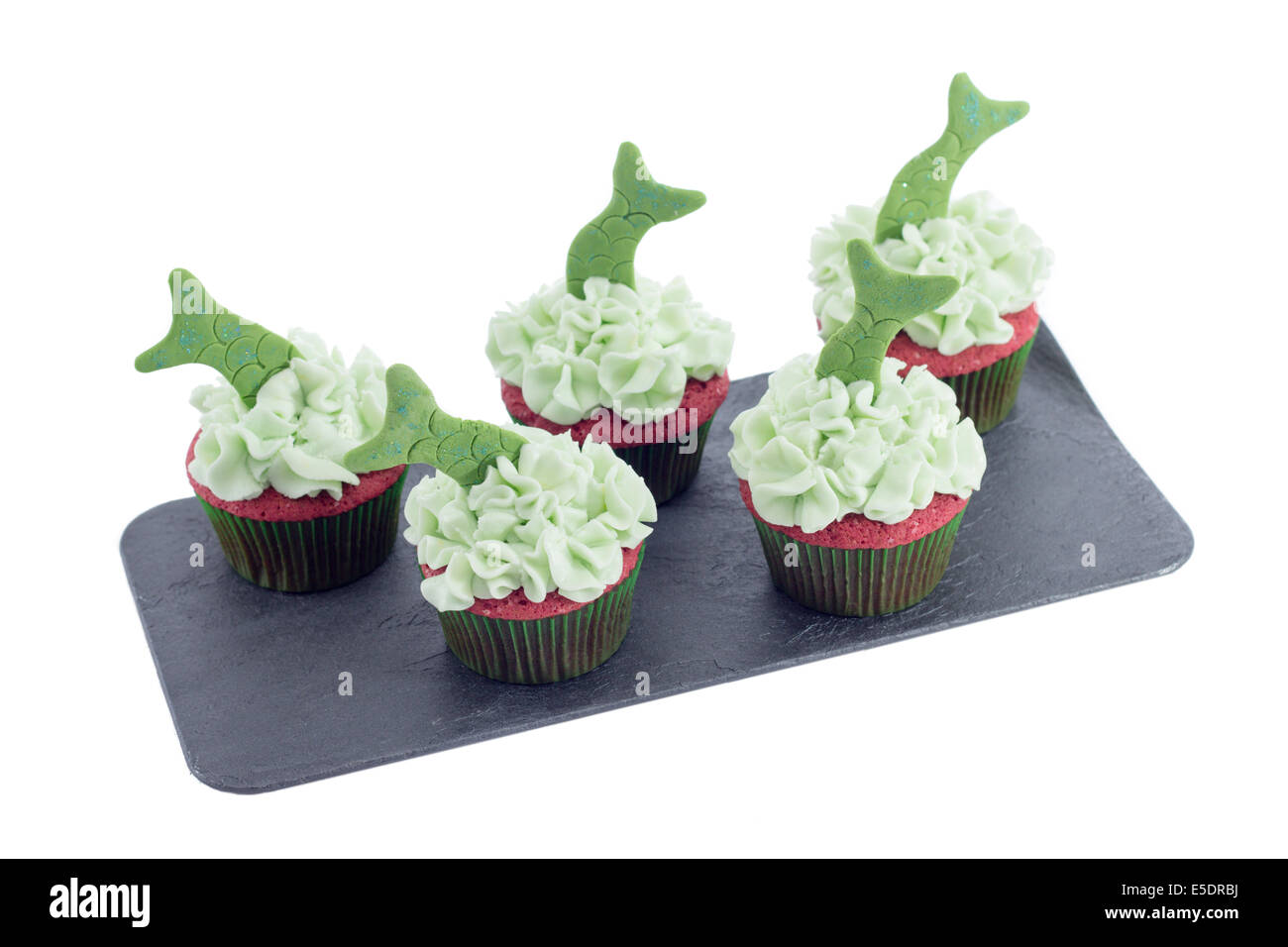 Cinq délicieux cupcakes avec glaçage vert et queues de poisson sur un plateau de schiste isolated on white Banque D'Images