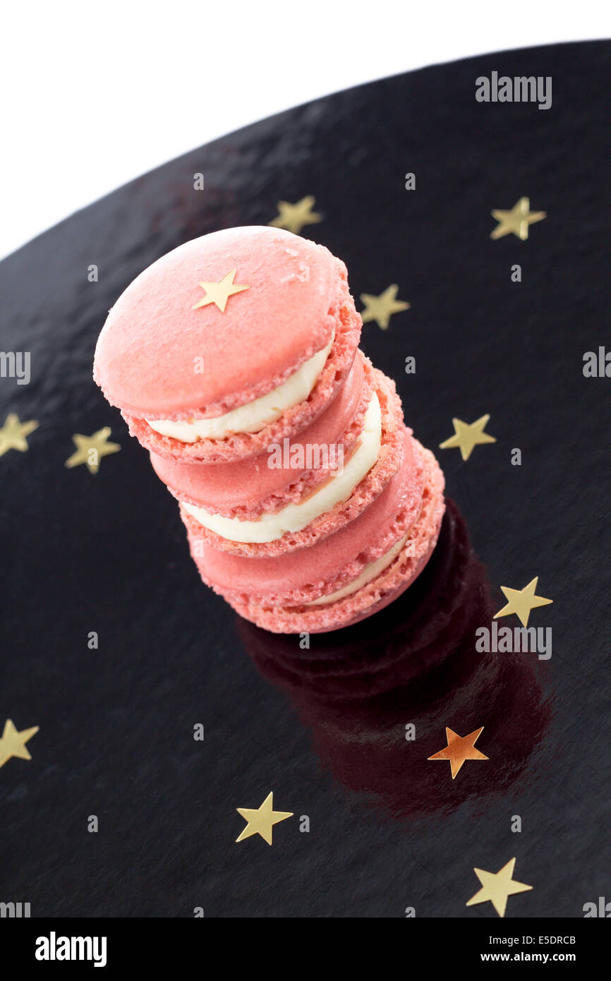 Trois macarons rose sur une surface brillante noire avec étoiles d'or Banque D'Images