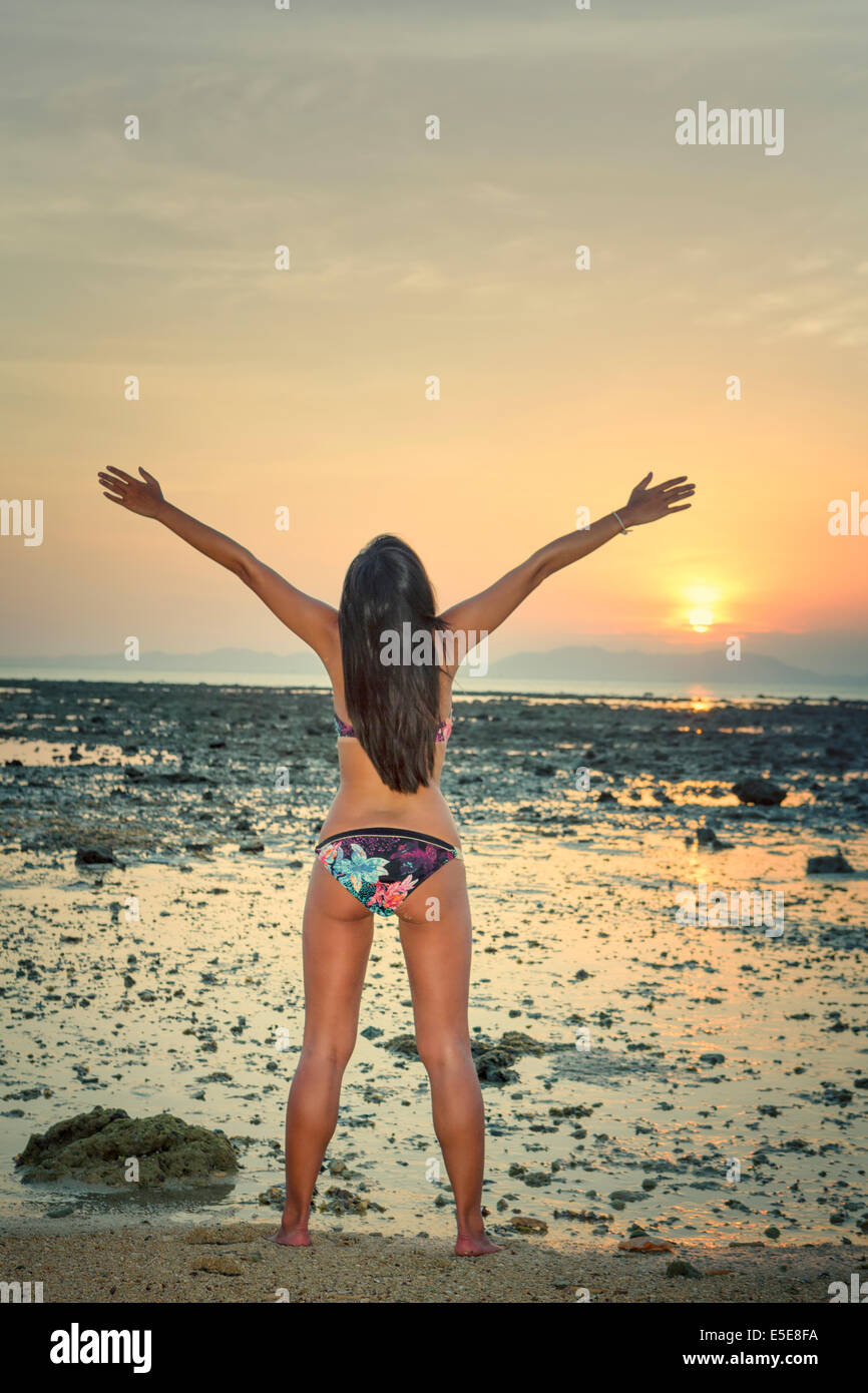 Une jeune femme les bras ouverts pour le lever du soleil sur une plage tropicale Banque D'Images