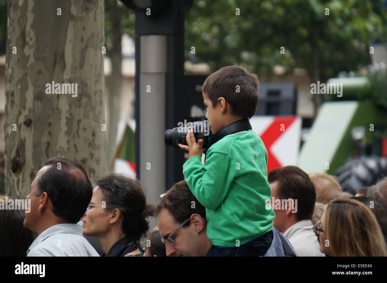 Un garçon en manteau vert assis sur les épaules de son père tenant une caméra comme un petit photographe sur le jour de la Bastille Paris Banque D'Images