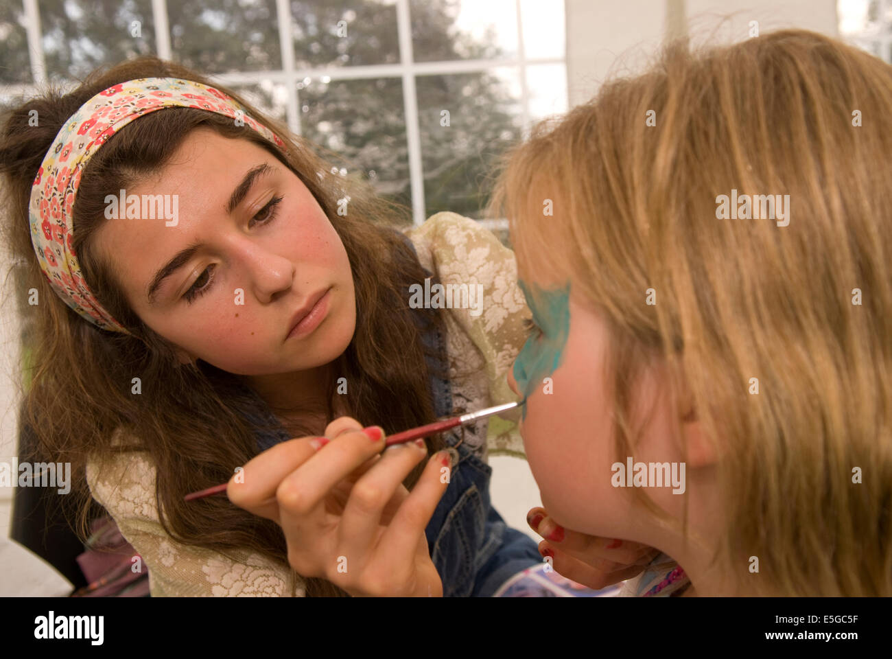 Jeune fille de 16 ans en peinture d'un visage du jeune lors d'une foire d'été, râteau, Hampshire, Royaume-Uni. Banque D'Images