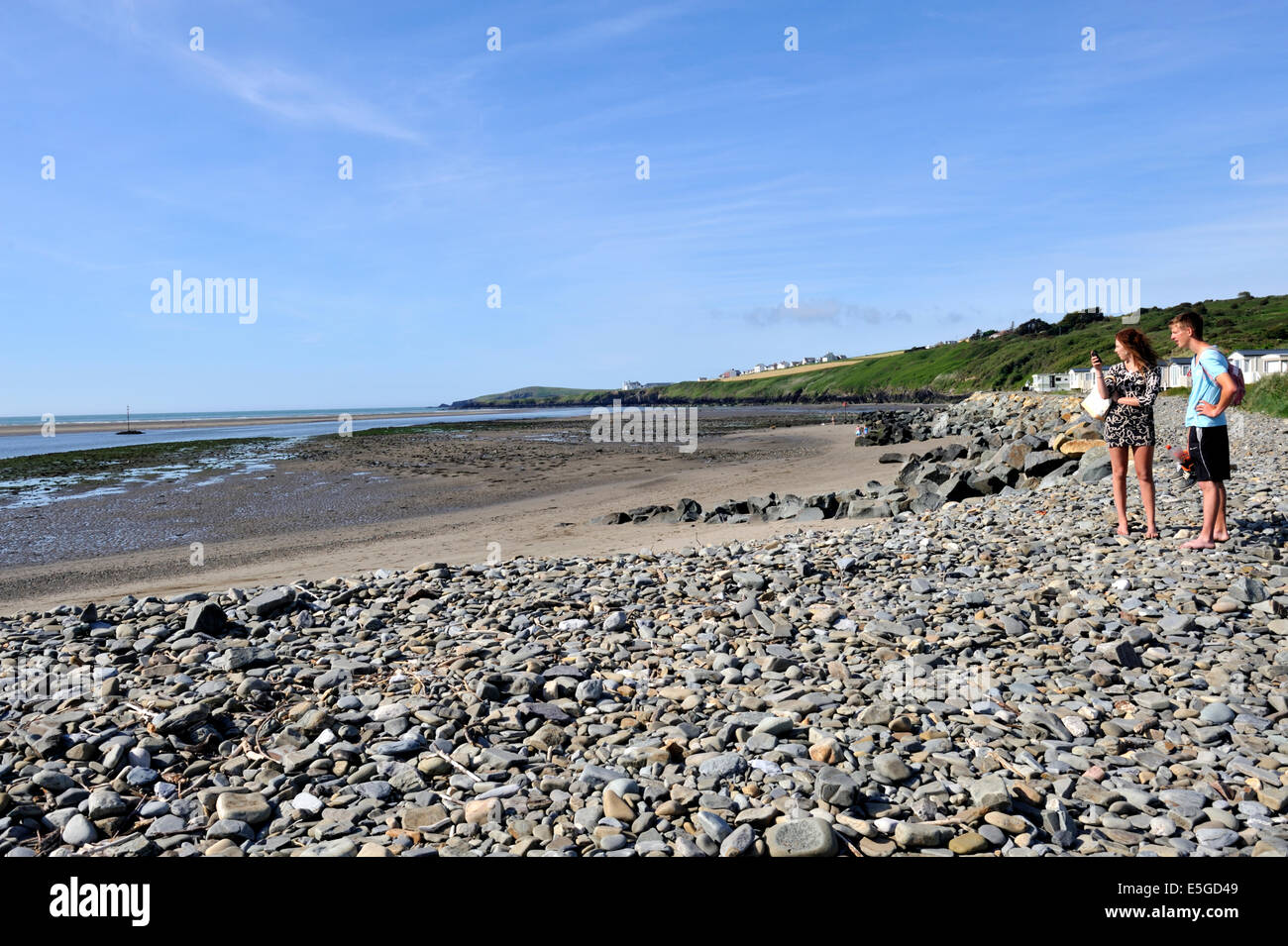 Jeune couple à la recherche sur les pavés de la plage par le correctif Traeth Caravan Park, Gwbert, Pembrokeshire Banque D'Images