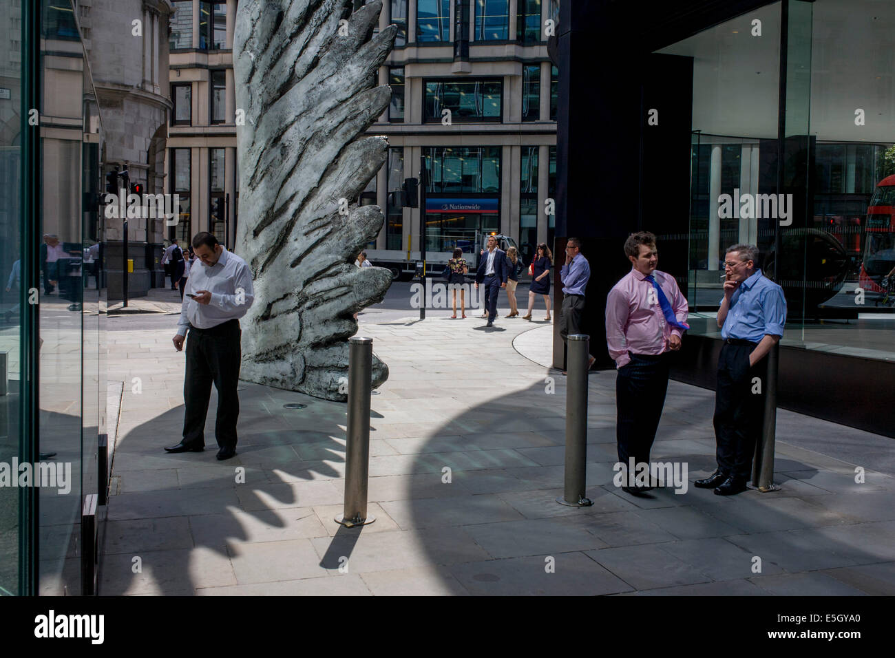 Les travailleurs de la ville de fumer des cigarettes par le géant de l'oeuvre une aile de bronze lors d'un midi de printemps dans le quartier financier de Londres. Comme la lumière se reflète sur les immeubles de bureaux à proximité, la foule à l'heure du déjeuner devant ce géant des illustrations sur leur façon de réunions et sandwicheries. Les dix mètres de haut est la sculpture en bronze par le président de la Royal Academy of Arts, Christopher Le Brun, commandé par Hammerson en 2009. Elle est appelée 'La Ville' de l'aile et a été jeté par Morris Singer, fondateurs de l'art réputé pour être la plus ancienne fonderie d'art dans le monde. Banque D'Images