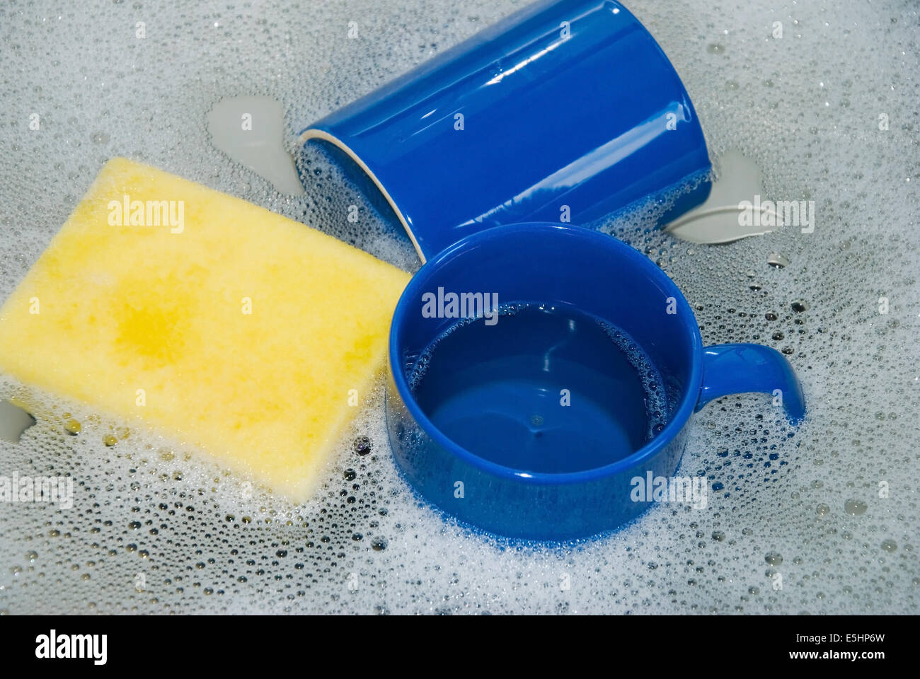 Deux tasses à café bleu avec une éponge jaune dans un évier de cuisine avec lave l'eau et la mousse, Close up Banque D'Images