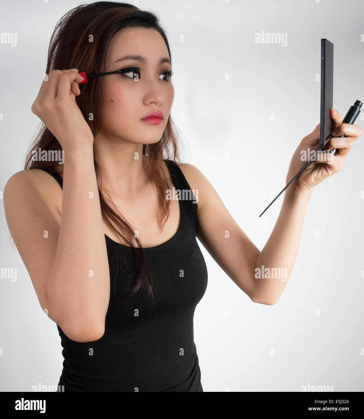 Cute Asian girl applying eye liner Banque D'Images
