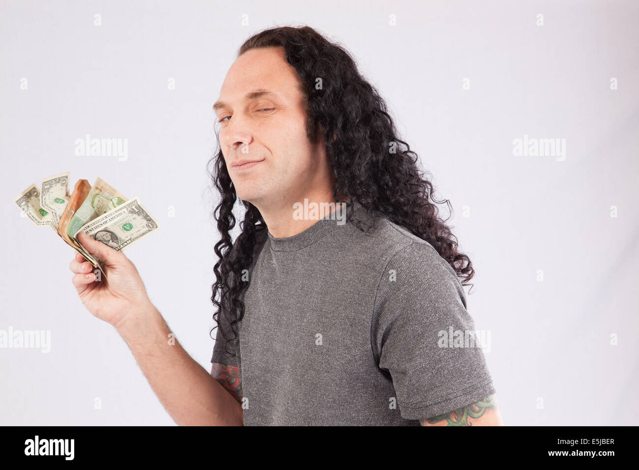 Homme de race blanche aux cheveux longs et chemise grise la détention d'espèces de différents pays, avec un sourire Banque D'Images