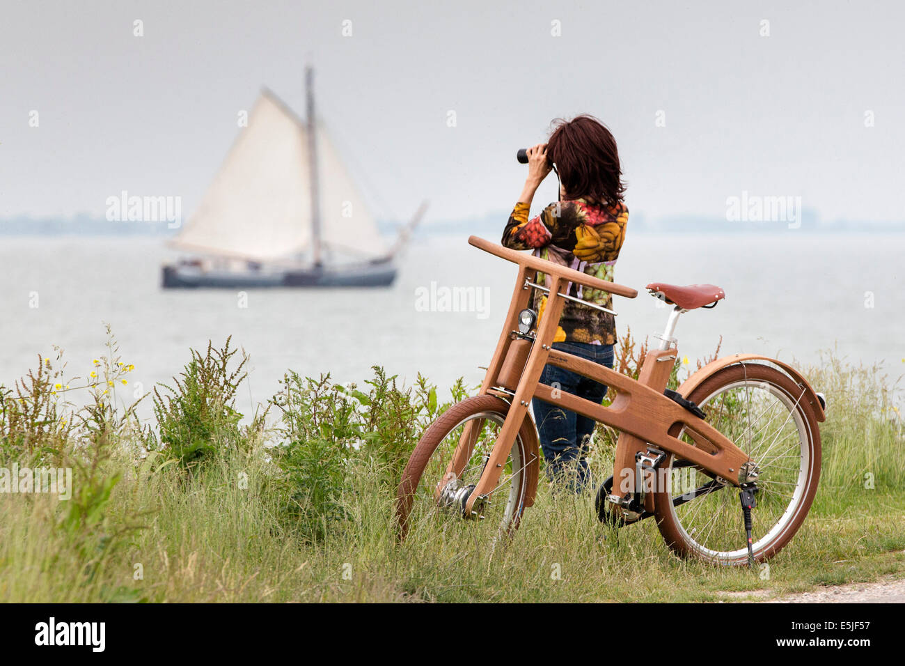 Pingjum Pays-bas, Rameau, Vélo. Le Dutch Design vélo en bois. Woman looking at bateau à voile avec des jumelles Banque D'Images