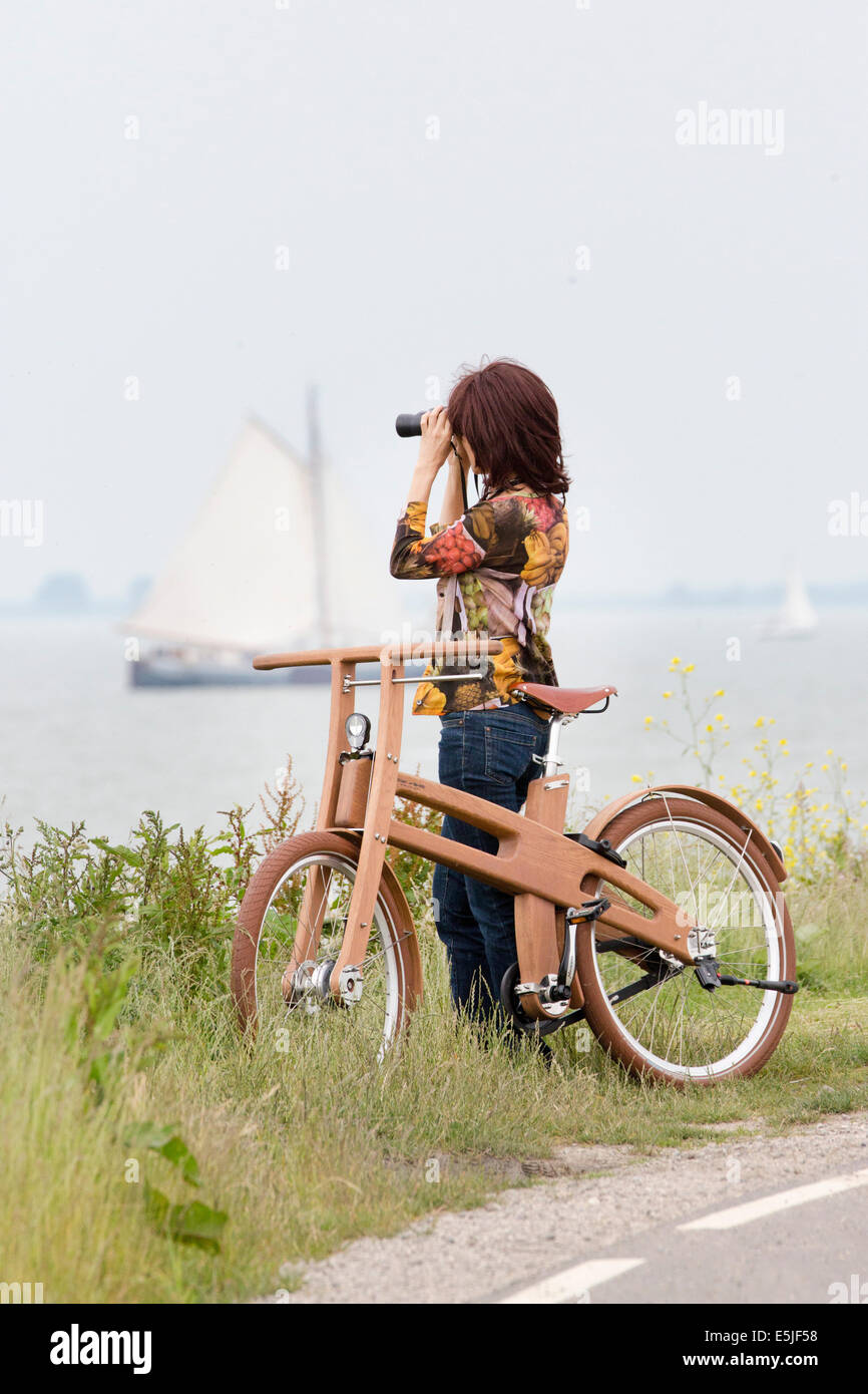 Pingjum Pays-bas, Rameau, Vélo. Le Dutch Design vélo en bois. Woman looking at bateau à voile avec des jumelles Banque D'Images