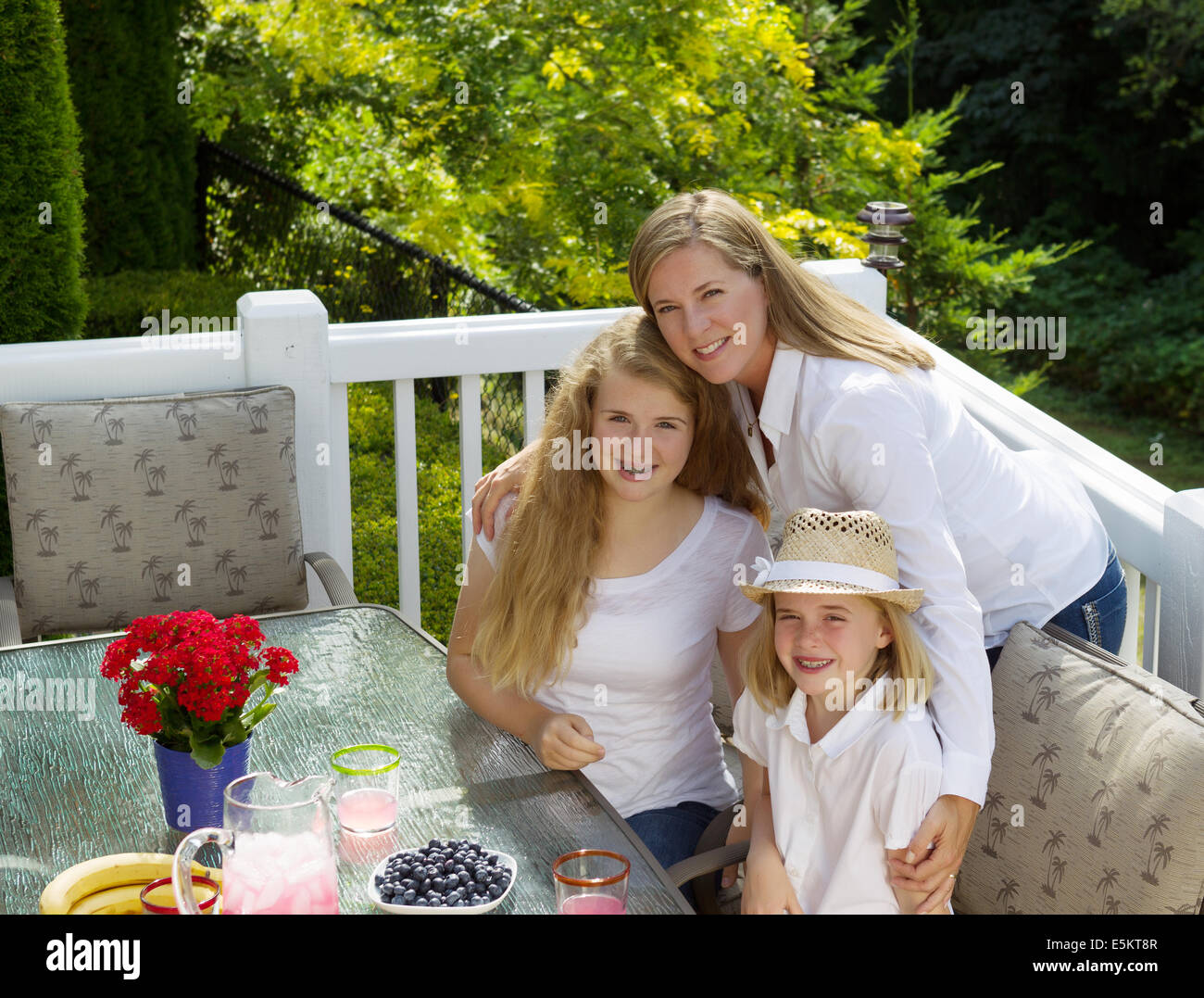 Vue avant du mature mother holding her two daughters tout en prenant un petit déjeuner en plein air, en été, sur un patio avec w Banque D'Images