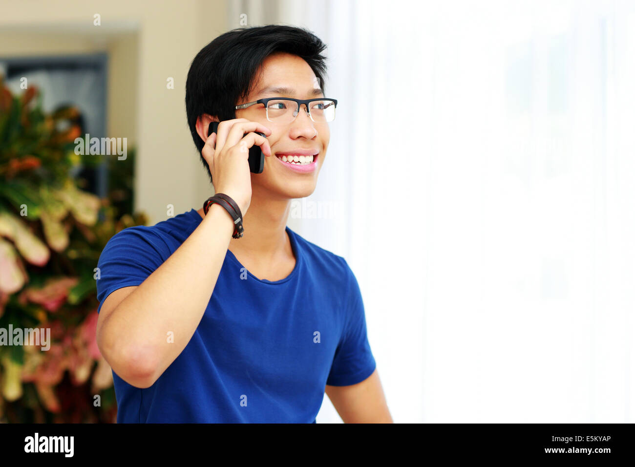 Smiling Asian man talking on the phone at home Banque D'Images