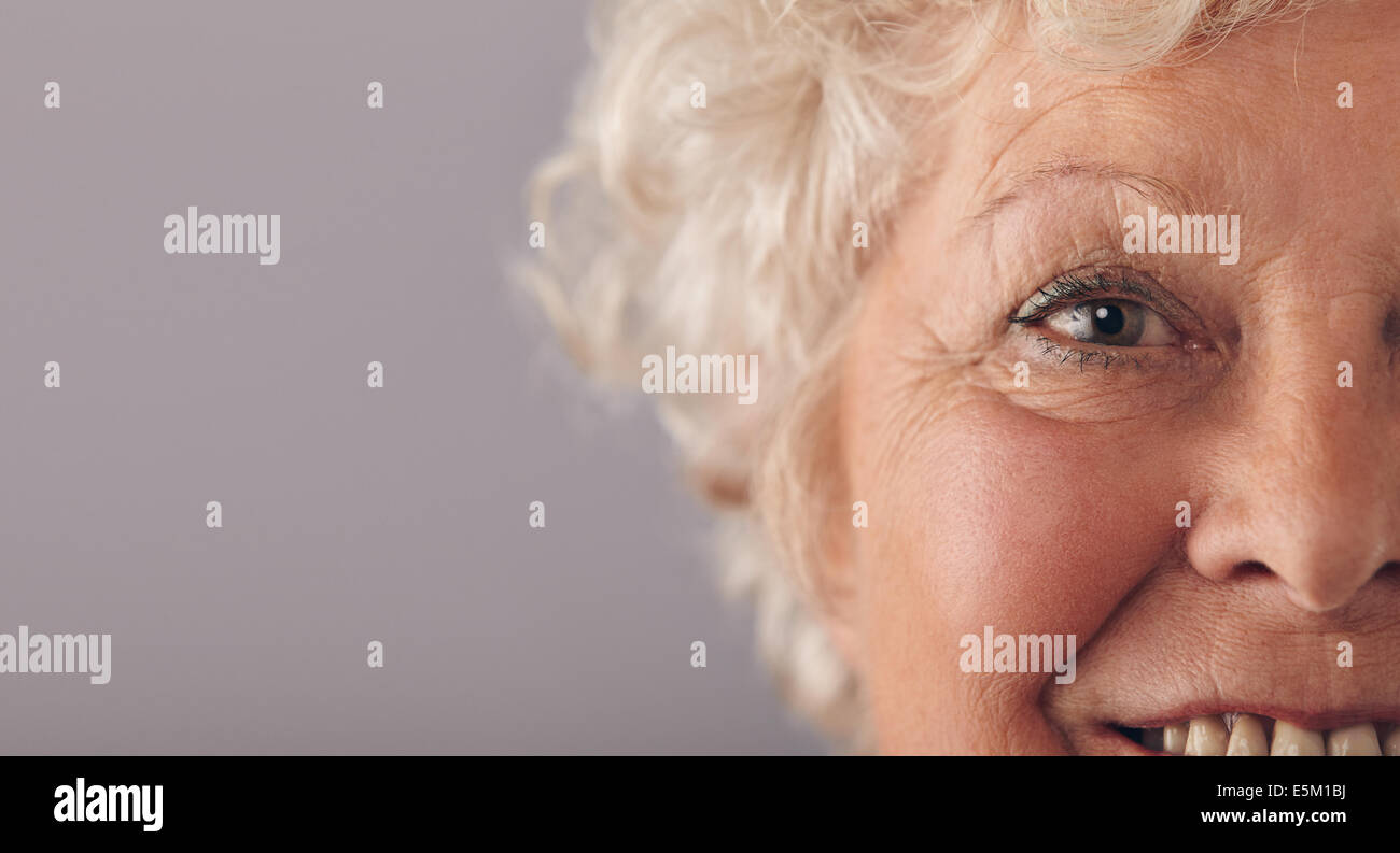 Partie de senior woman face avec l'accent sur les yeux gris. Vieille Femme face close-up with copy space sur contre fond gris. Banque D'Images