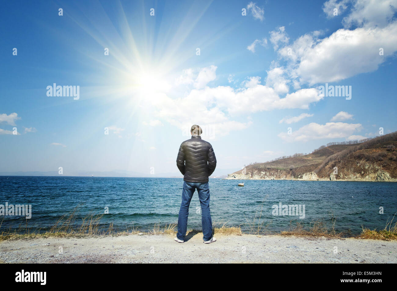 Homme dans un manteau noir se tenant sur la mer ciel soleil d'arrière-plan Banque D'Images
