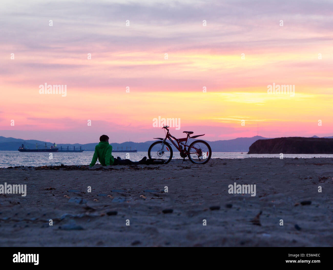 Jeune homme assis sur la plage au coucher du soleil Banque D'Images