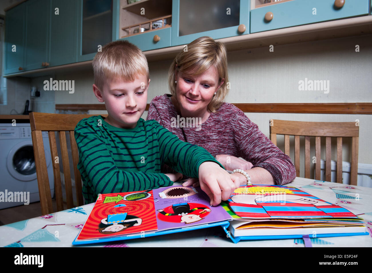 Maman avec son fils de 8 910 alors qu'il dessine et regarde à travers un livre Banque D'Images