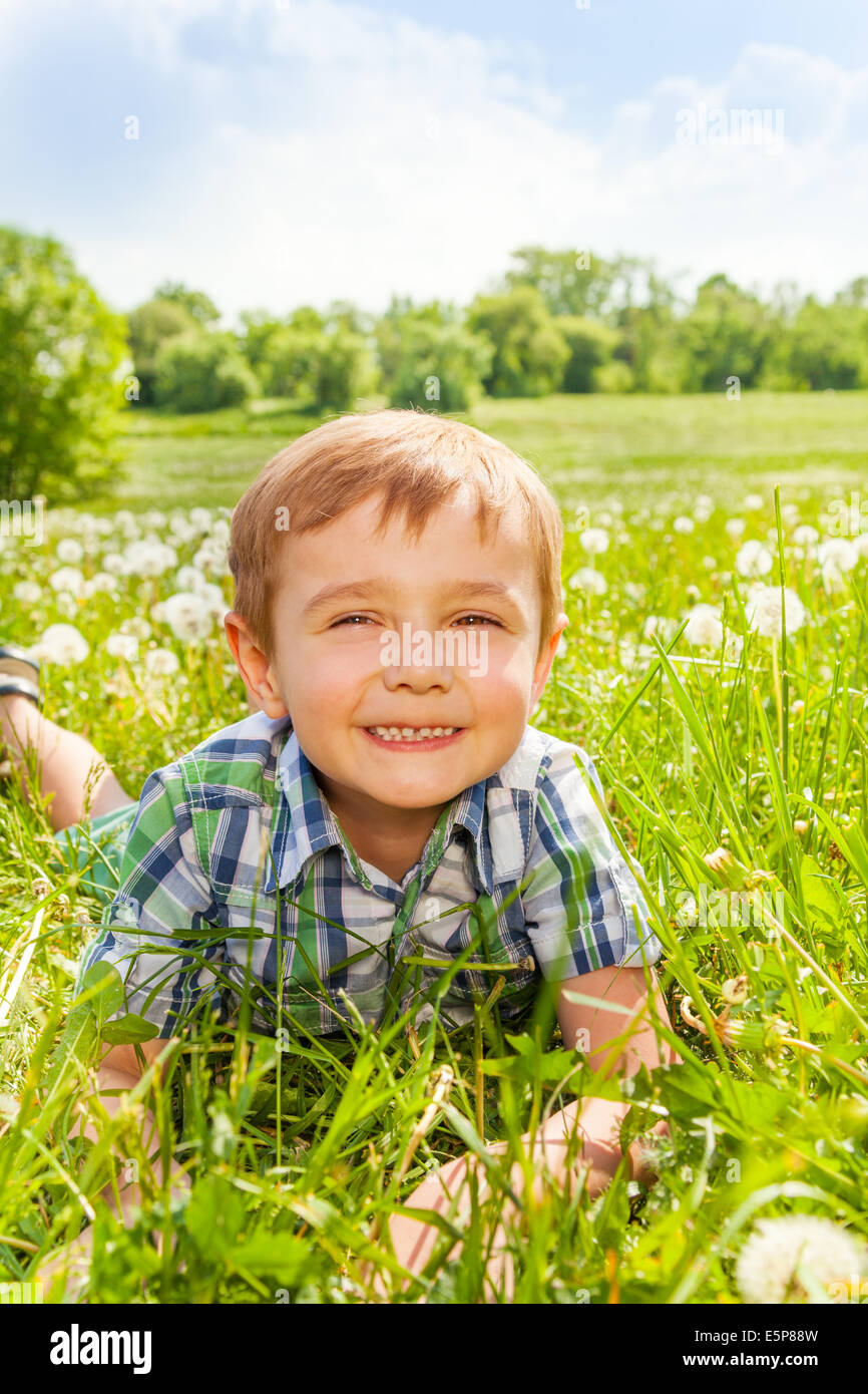 Gentil garçon sourit portant sur une herbe Banque D'Images