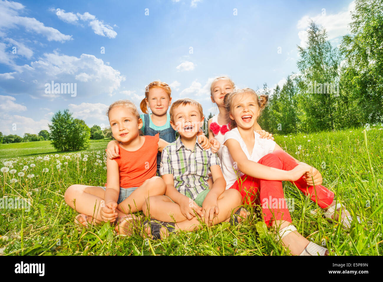 Groupe d'enfants rire assis sur une herbe Banque D'Images