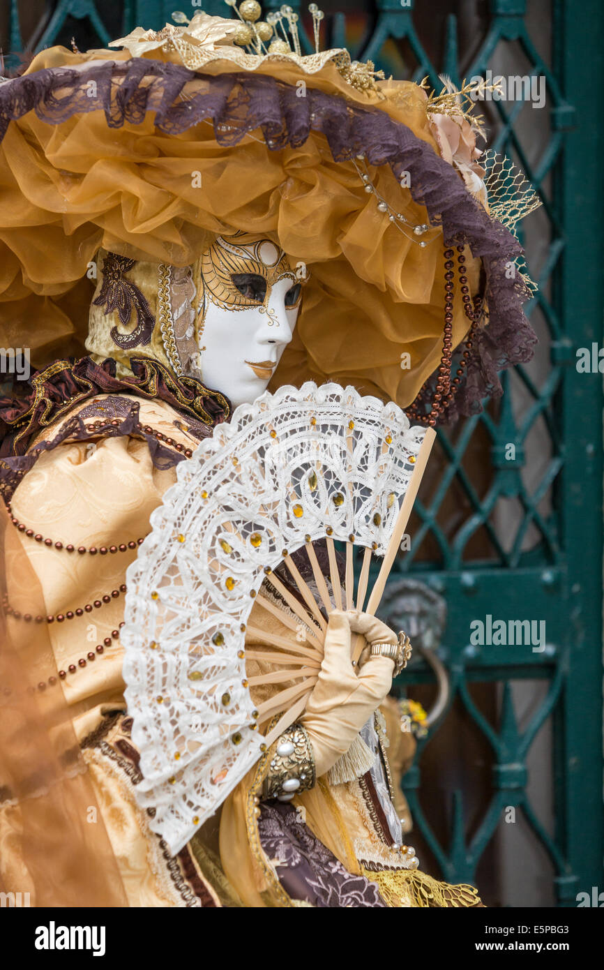 Femme en costume d'or élaborée & dentelle blanche ventilateur devant la porte en fer forgé vert, San Zaccaria pendant le carnaval, Venise. Banque D'Images