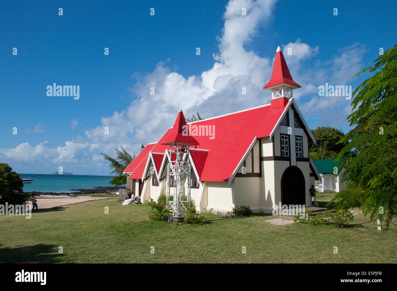 Un couple de jeunes mariés qui pose pour des photos à l'extérieur de l'église au toit rouge à Cap Malheureux sur la côte nord-ouest de l'Ile Maurice Banque D'Images