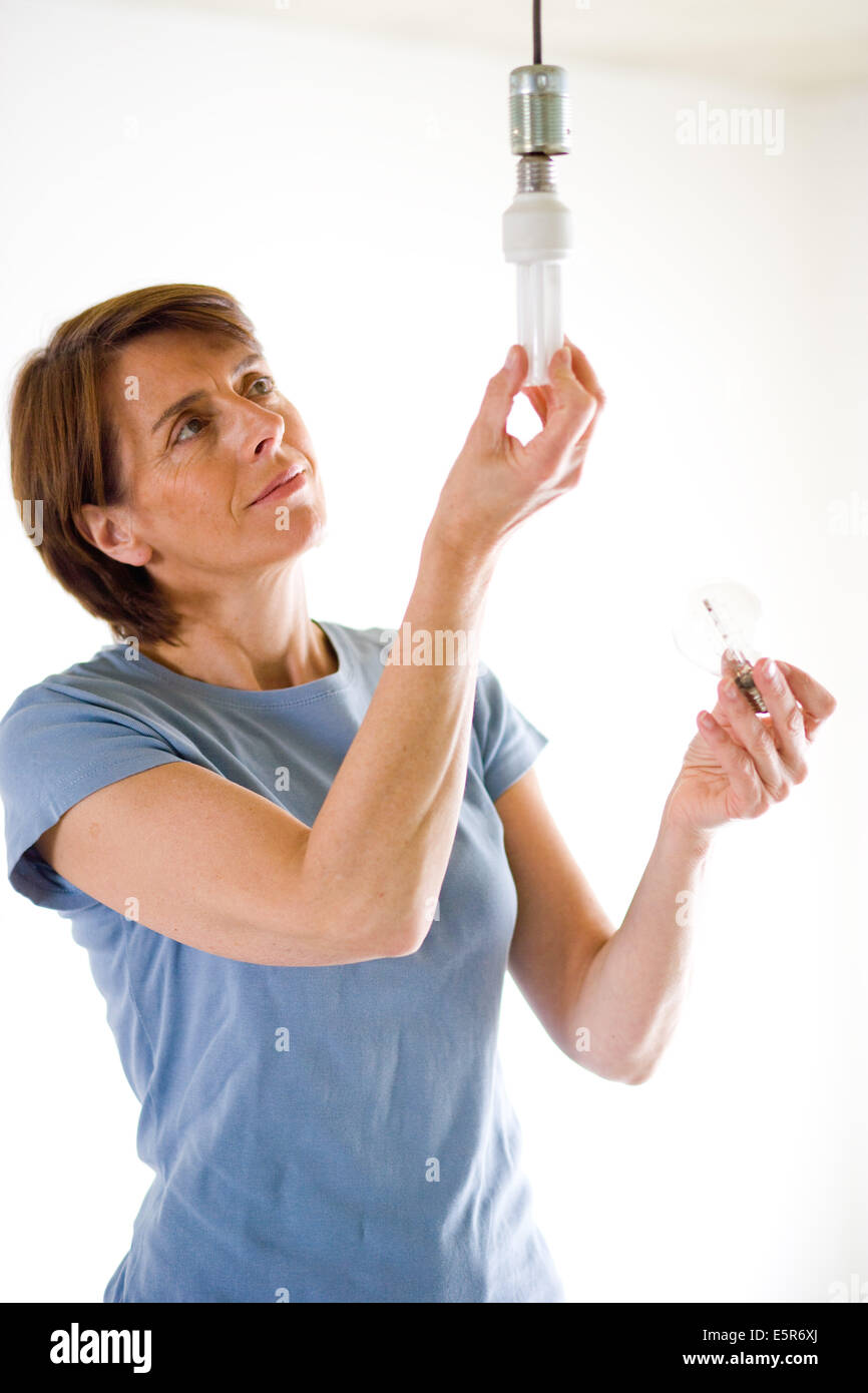 Femme mettant un energy saving lightbulb. Banque D'Images
