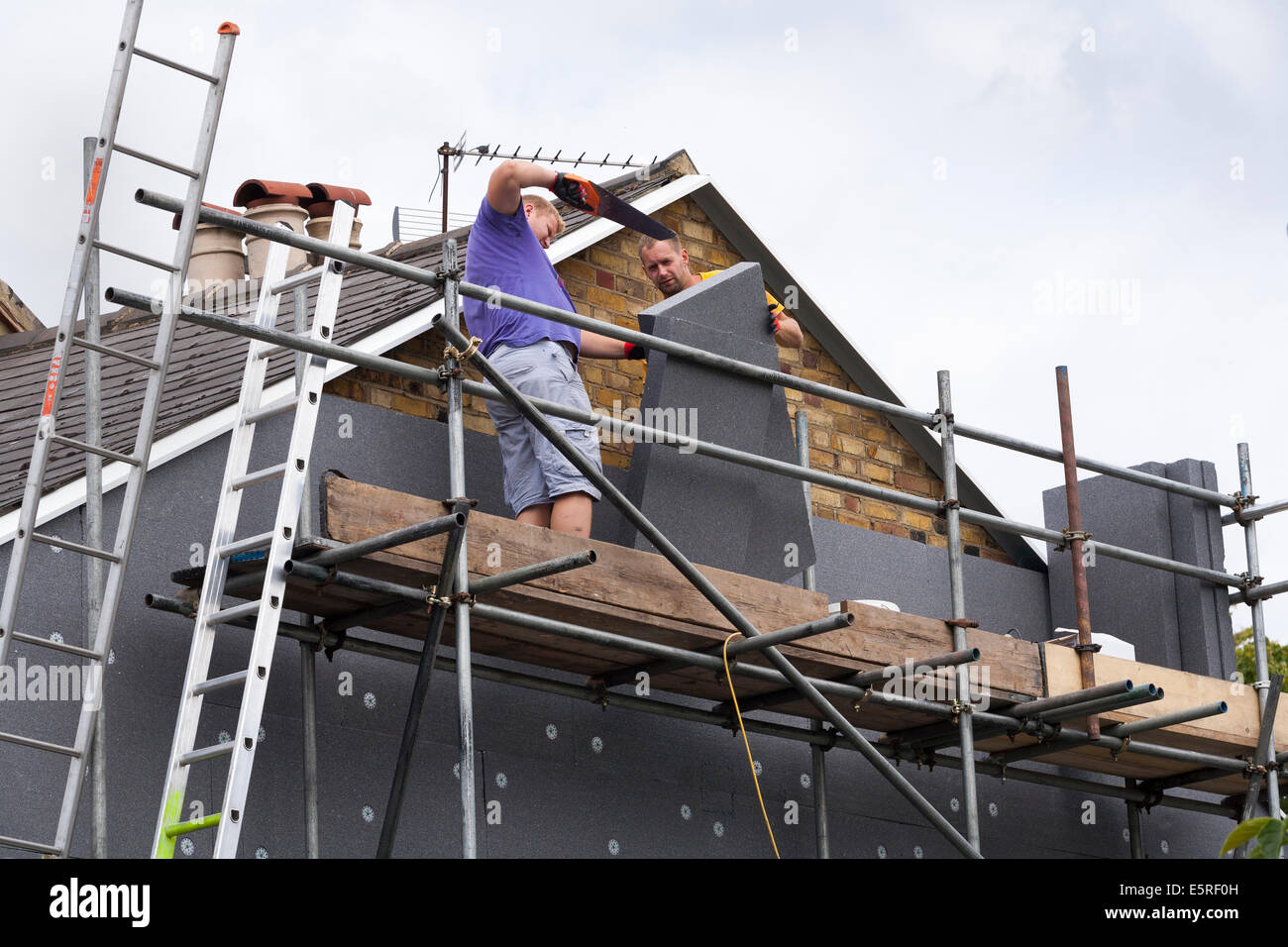 Constructeurs attachant / adaptant l'isolation murale solide en mousse rigide ( SWI ) feuilles / panneaux / planches à l'extrémité du pignon de la maison mitoyenne victorienne Royaume-Uni Banque D'Images
