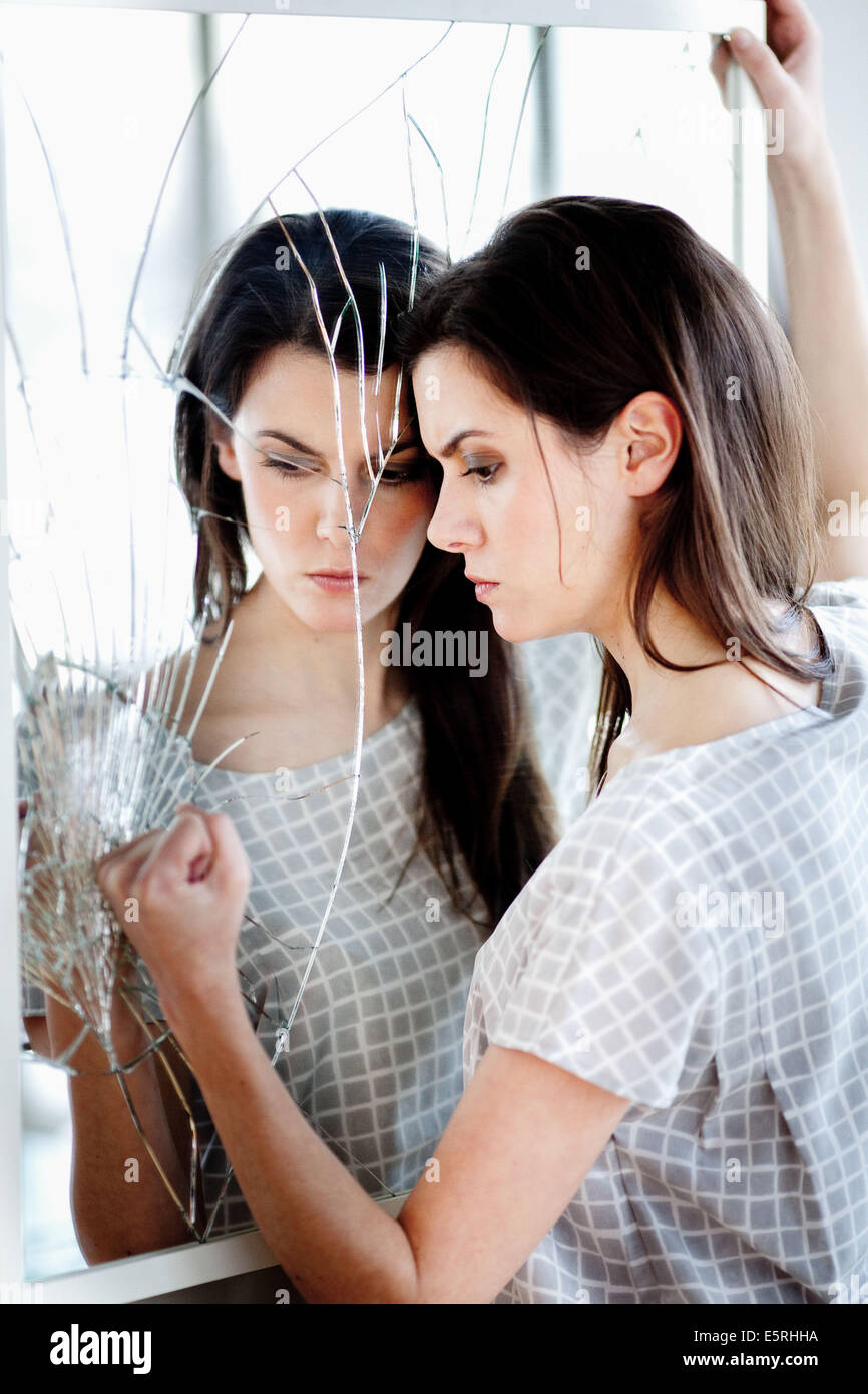 Femme en colère en face d'un miroir brisé. Banque D'Images
