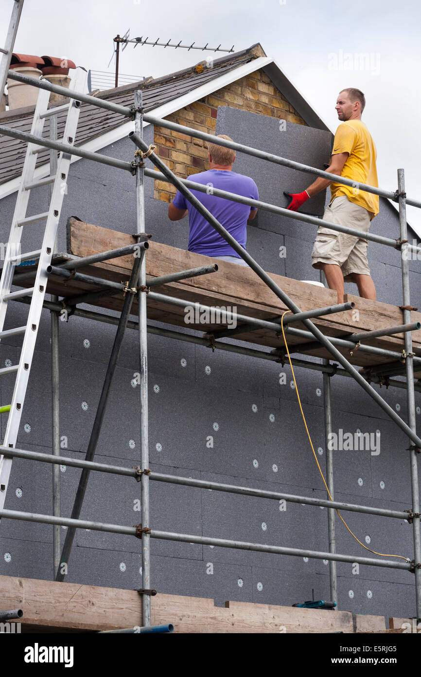 Constructeurs attachant / adaptant l'isolation murale solide en mousse rigide ( SWI ) feuilles / panneaux / planches à l'extrémité du pignon de la maison mitoyenne victorienne Royaume-Uni Banque D'Images