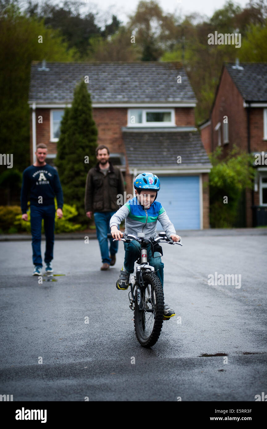 Garçon apprendre à conduire un vélo avec Boy apprendre à rouler à vélo avec les parents masculins en arrière-plan Banque D'Images