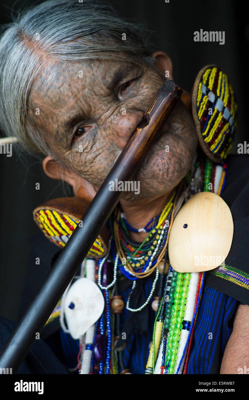 85-ans femme Chin (Yun) Eian jouer flûte, l'État de Chin, Mindat, Myanmar. Son visage est tatoué, traditionnelles chez les Chin Banque D'Images