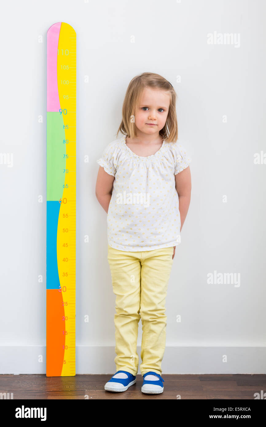 Fillette de 3 ans mesurant elle-même contre une jauge de hauteur. Banque D'Images