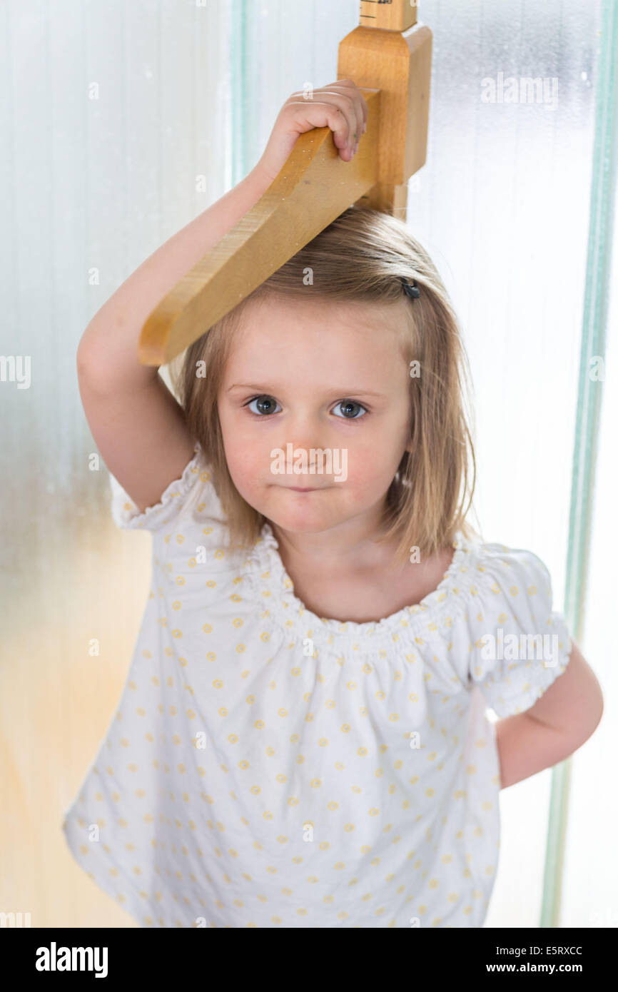 Fillette de 3 ans mesurant elle-même contre une jauge de hauteur. Banque D'Images