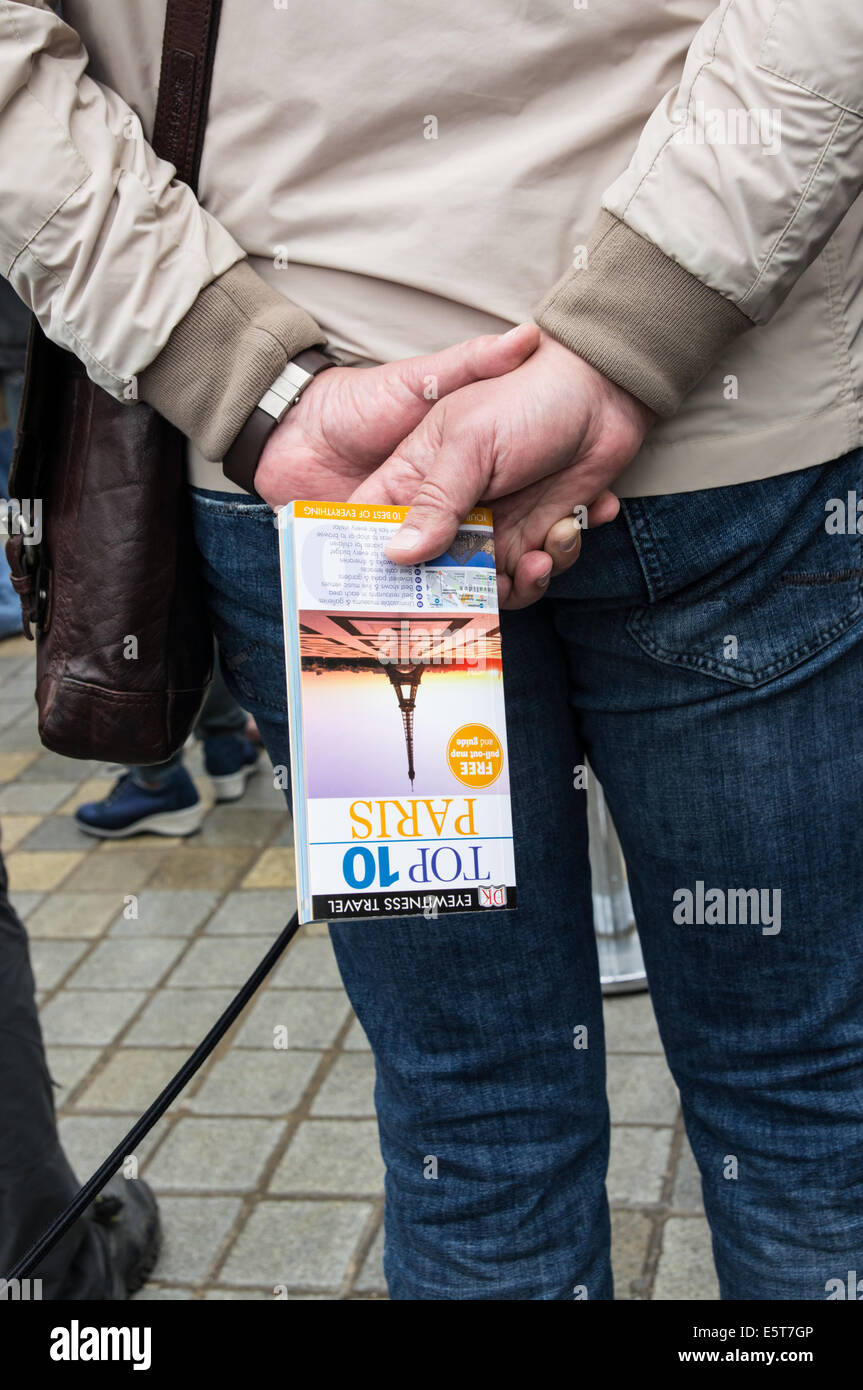 Visiteur tenant la file d'attente du guide de voyage de Paris à l'entrée du musée du Louvre Paris, France Banque D'Images