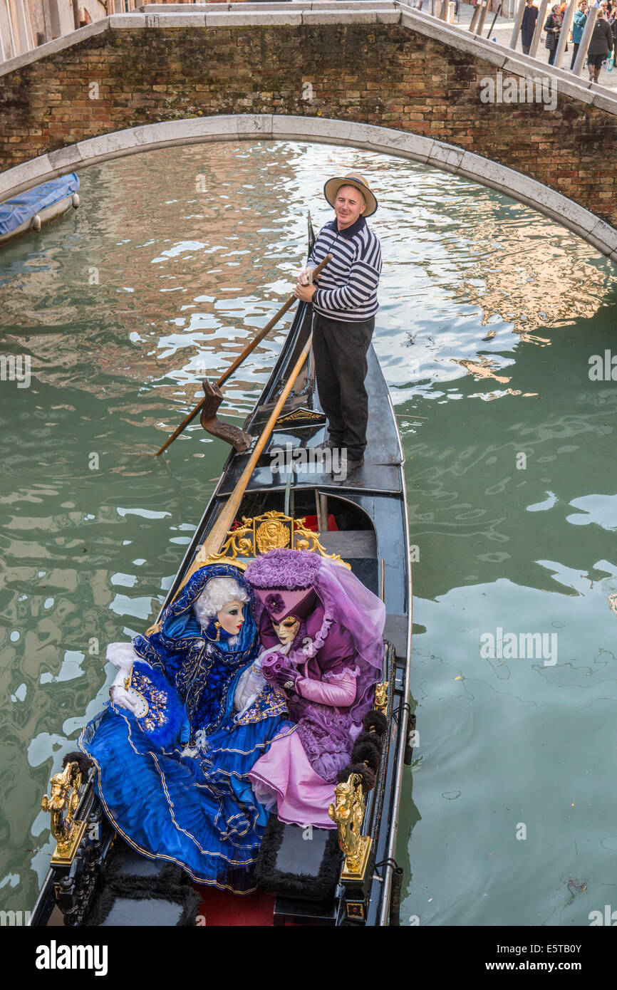 Les femmes dans des poteaux Gondolier bleu et violet costumes en gondole sur un canal latéral pendant le Carnaval de Venise. Banque D'Images
