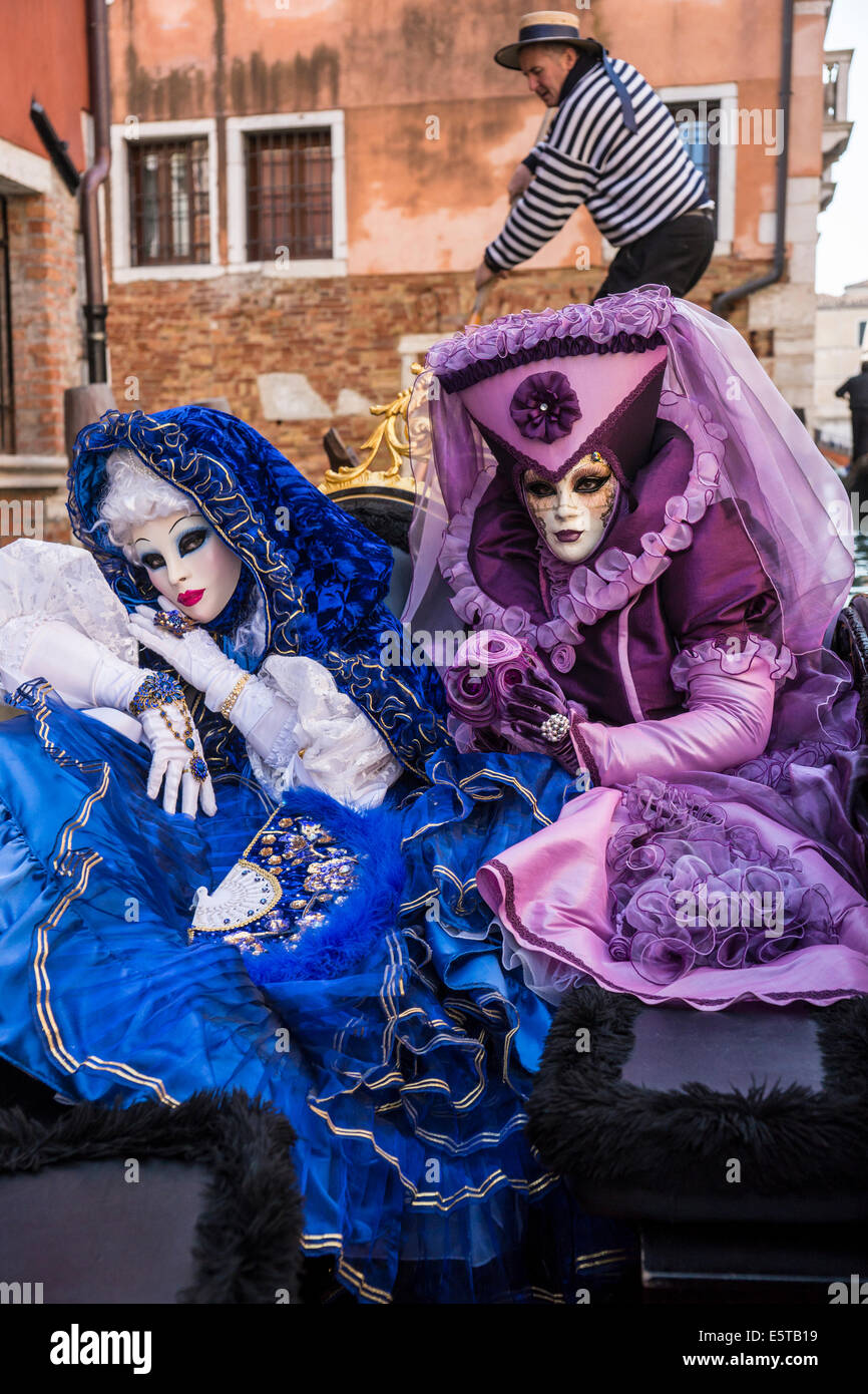 Les femmes dans des poteaux Gondolier bleu et violet costumes en gondole sur un canal latéral pendant le Carnaval de Venise. Banque D'Images