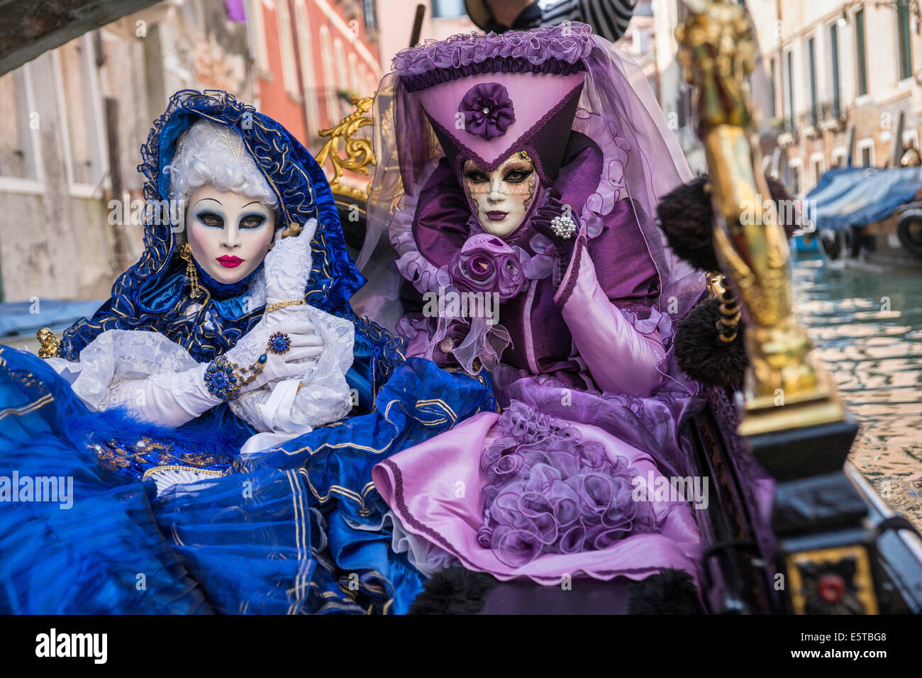 Les femmes dans des costumes bleus et violets à une télécabine vers le bas un canal latéral pendant le carnaval de Venise. Banque D'Images