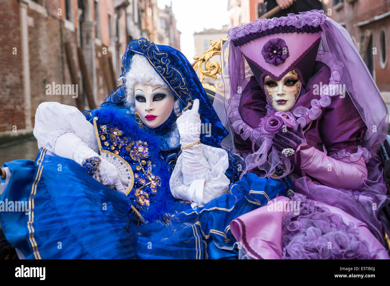 Les femmes dans des costumes bleus et violets à une télécabine vers le bas un canal latéral pendant le carnaval de Venise. Banque D'Images