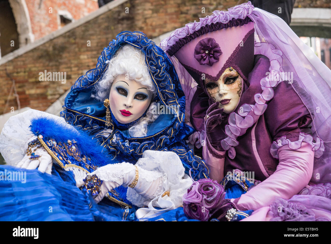 Les femmes dans des costumes bleus et violets à une télécabine vers le bas un canal latéral pendant le carnaval de Venise. Banque D'Images