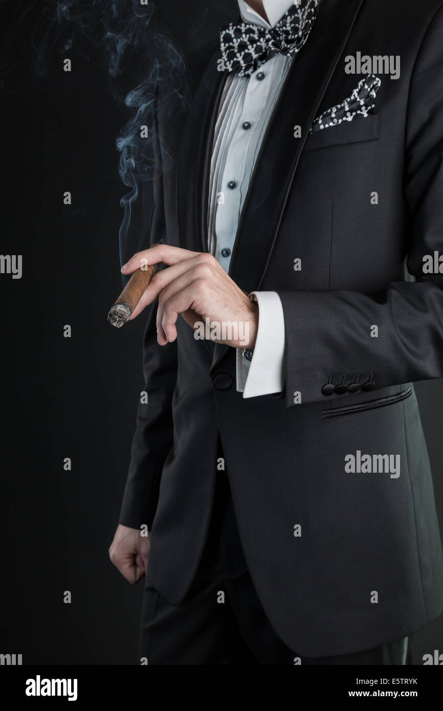 Homme dans un costume noir tenant un cigare dans une main gauche Banque D'Images