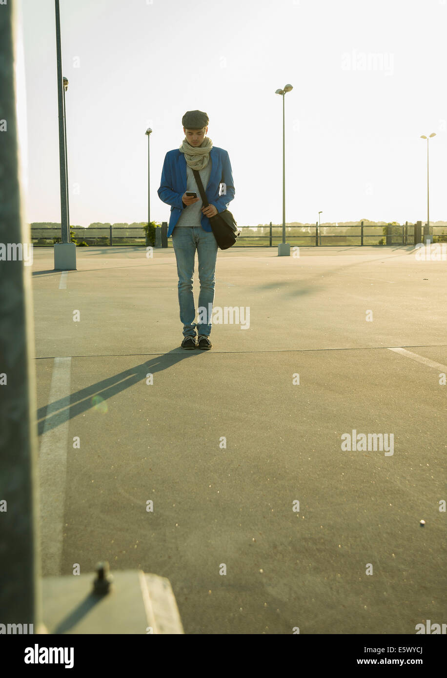 Jeune homme avec le smartphone en vous promenant à travers parking vide Banque D'Images