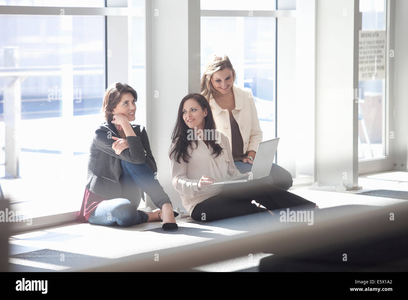 Trois businesswomen sitting on floor with laptop in conference centre Banque D'Images