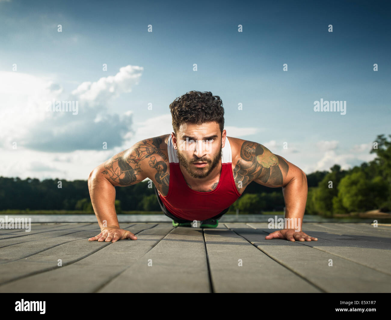 Niveau Surface portrait of young man doing push ups on lake pier Banque D'Images