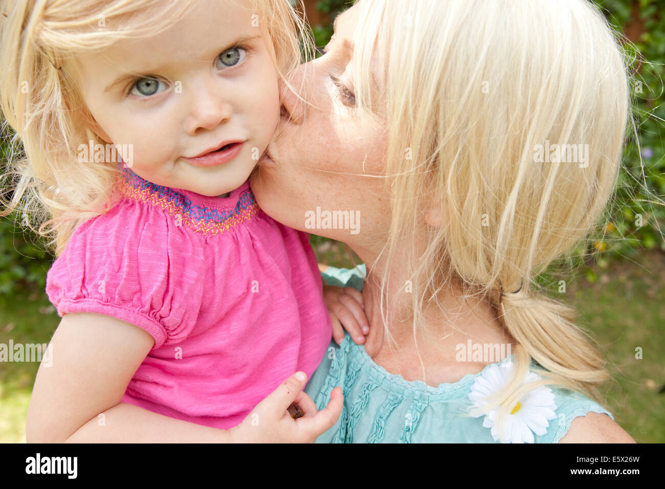 Close up of young adult mother kissing toddler daughter in garden Banque D'Images