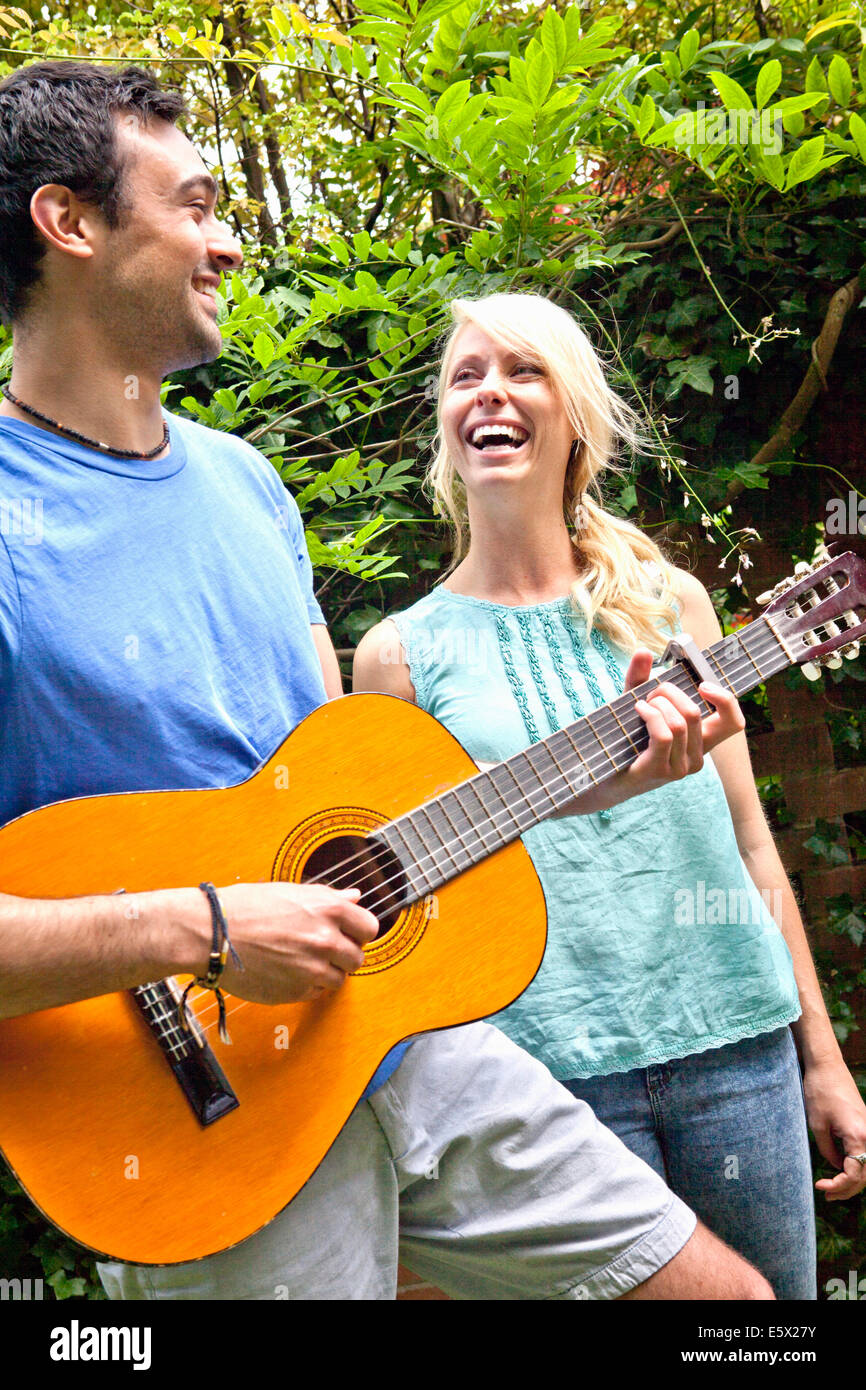 Jeune homme jouant de la guitare acoustique en jardin pour l'amie Banque D'Images