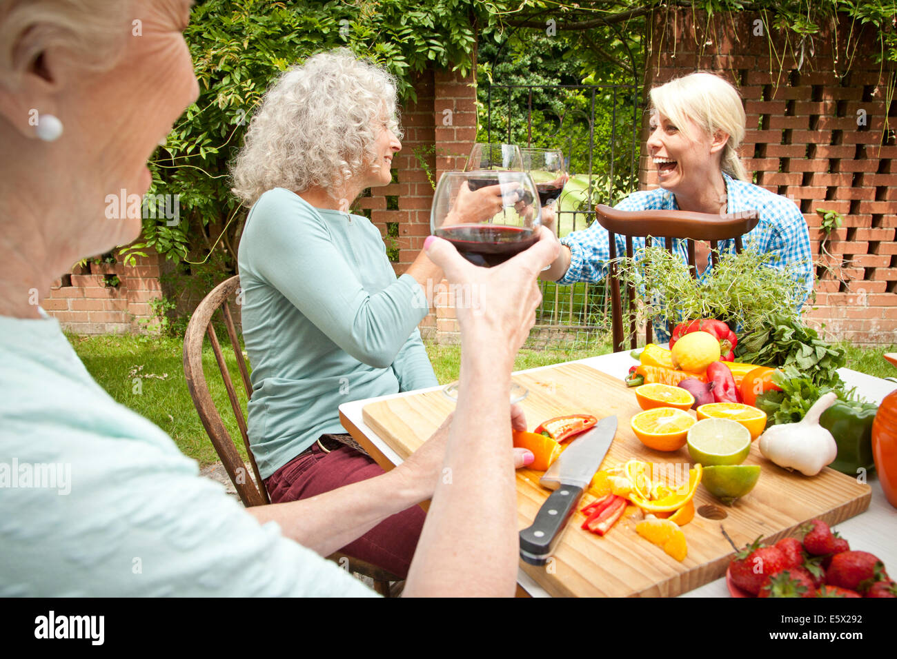 Les femmes qui élèvent trois générations d'un verre de vin rouge tout en préparant la nourriture à table de jardin Banque D'Images Les femmes qui élèvent trois générations d'un verre de vin rouge tout en préparant la nourriture à table de jardin Banque D'Images