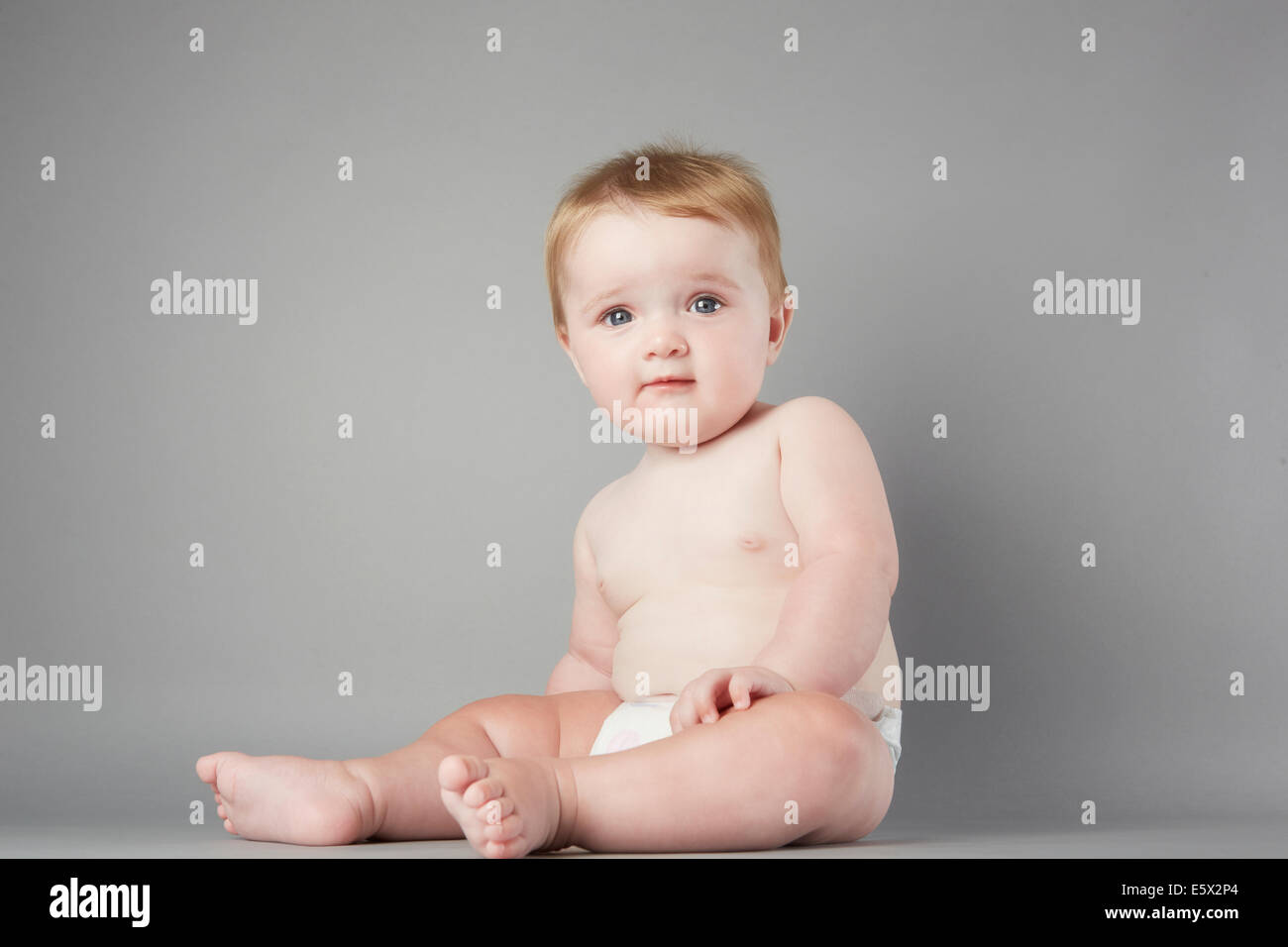 Studio portrait of baby girl sitting up perplexe Banque D'Images